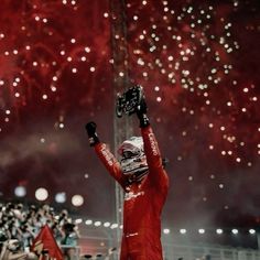 a man in a red suit holds up his hands as fireworks go off behind him