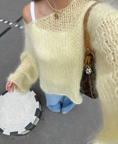a woman wearing a yellow sweater and holding a purse