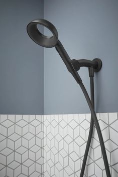 a black shower head in a bathroom next to a white tiled wall with grey walls