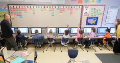 a classroom full of students with their hands up in front of computer screens and desks