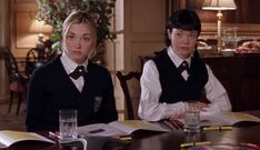 two young women sitting at a table with books and glasses on top of each other