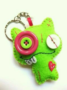 a green stuffed animal keychain with a pink button on it's face