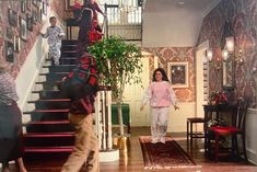 two people are walking up the stairs in a house with red carpet and patterned walls