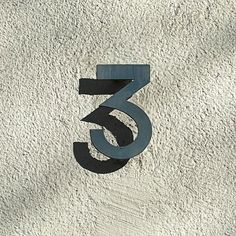 the number three is made out of metal and sits on a white stucco wall in front of it