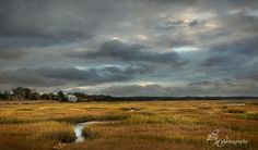 the sky is dark and cloudy over an open field with a stream running through it