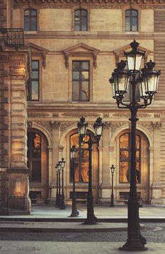 an old fashioned lamp post in front of a building with windows and lights on it