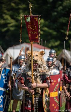 men in roman armor with dogs on their backs and one man holding a sign that says,