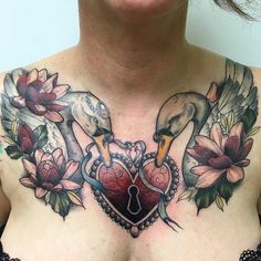 a woman's chest with flowers and two swans on it, holding a heart