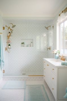 a white tiled bathroom with gold accents and blue towels hanging on the shower wall, along with two sinks