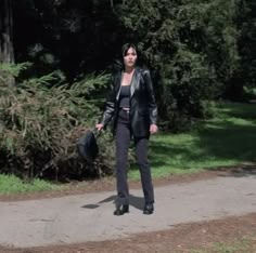 a woman walking down a dirt road with trees in the background