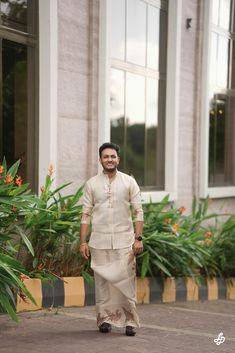 a man standing in front of a building wearing a white shirt and tan dhoti