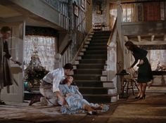 two women and a man standing in front of a staircase with stairs leading up to the second floor