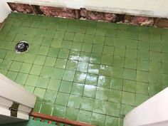 an overhead view of a bathroom with green tile flooring and exposed pipes in the wall