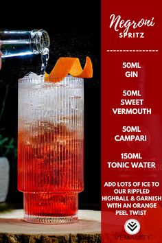 a tall glass filled with red liquid and an orange slice being poured into the drink