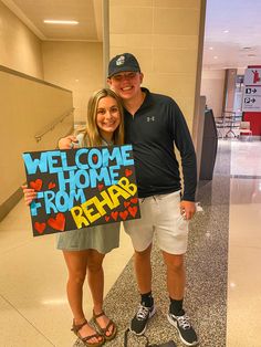 a man and woman standing next to each other holding a welcome home sign