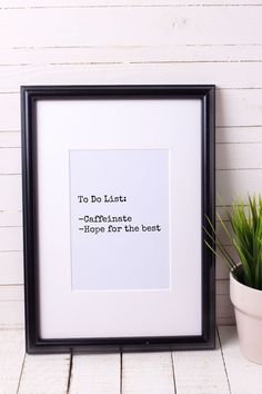 a black framed print with the words to do list on it next to a potted plant
