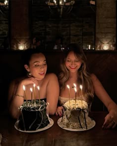 two beautiful women sitting in front of a cake with candles