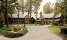a large house with lots of trees in the front yard and driveway leading to it