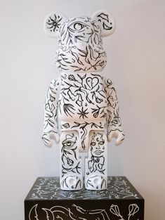 a black and white teddy bear sitting on top of a wooden box with writing all over it