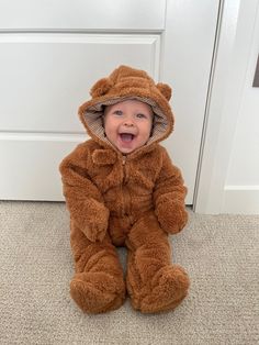 a baby in a teddy bear costume sitting on the floor next to a white door