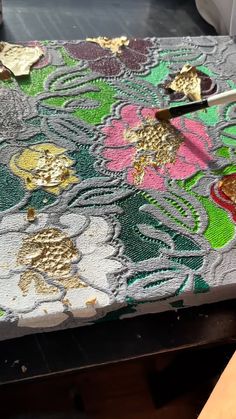 someone is using scissors to cut the fabric with gold and pink flowers on it,