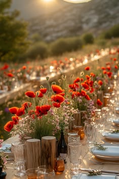 a long table with plates and vases filled with red flowers on top of it