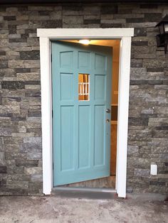 a blue door is open in front of a stone wall and light fixture on the side