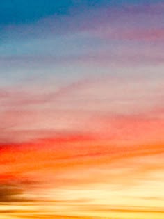 an airplane is flying in the sky at sunset or sunrise with clouds and blue, yellow, red and orange colors