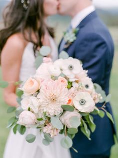 a bride and groom kissing in front of a green field with flowers on their wedding day