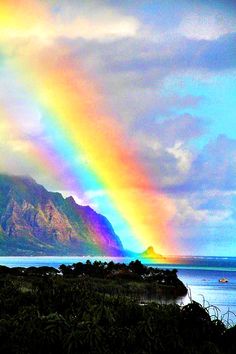 a rainbow shines brightly in the sky over water and mountains with boats on it