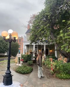 a woman standing in front of a house next to a lamp post with flowers on it