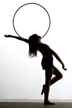 a woman is doing tricks with a hula hoop in front of a white wall