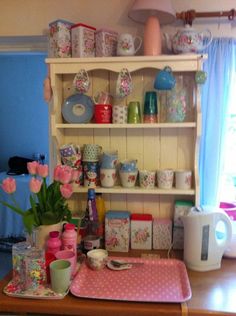 a kitchen counter topped with lots of dishes and cups next to a window filled with pink tulips