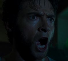 a man with his mouth open in the dark, looking at something and making an angry face