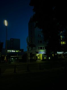 an empty street at night with buildings lit up in the background and trees on both sides