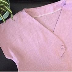 a close up of a pink shirt with a plant in the corner next to it