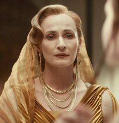 a woman in a gold dress and veil looking at another woman's face with her eyes closed