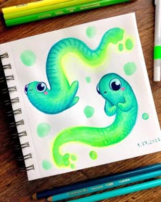a drawing of two blue and green snakes on a piece of paper with colored pencils next to it
