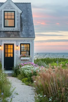 a small house sitting on top of a lush green field next to the ocean at sunset