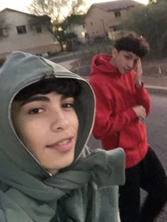 two young men are standing on the side of the road and one is wearing a hoodie