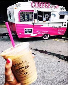 a person holding up a drink in front of a pink and white food truck on the street