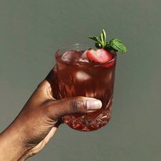 a hand holding up a drink with a strawberry on the top and green leafy garnish