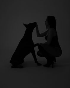 a woman kneeling down next to a dog in the dark with her hand on it's paw