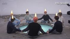 five people sitting in a circle with candles on their heads and one person holding the other's hand