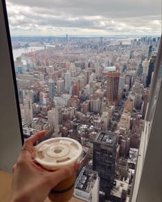 a person holding up a drink in front of a window overlooking a cityscape