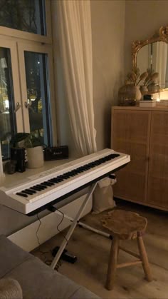 a white piano sitting in front of a window next to a wooden table and chair