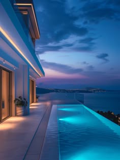 an outdoor swimming pool at night with lights on the side and ocean in the background