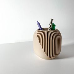 a pen holder with two pens in it on a white surface, next to a wall