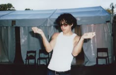 a man in white shirt and sunglasses standing next to a blue tarp covered tent
