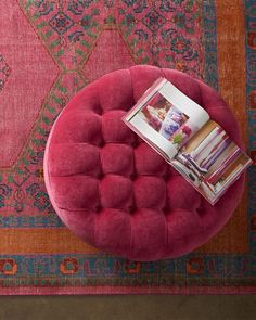 a pink ottoman sitting on top of a rug next to a table with magazines in it
